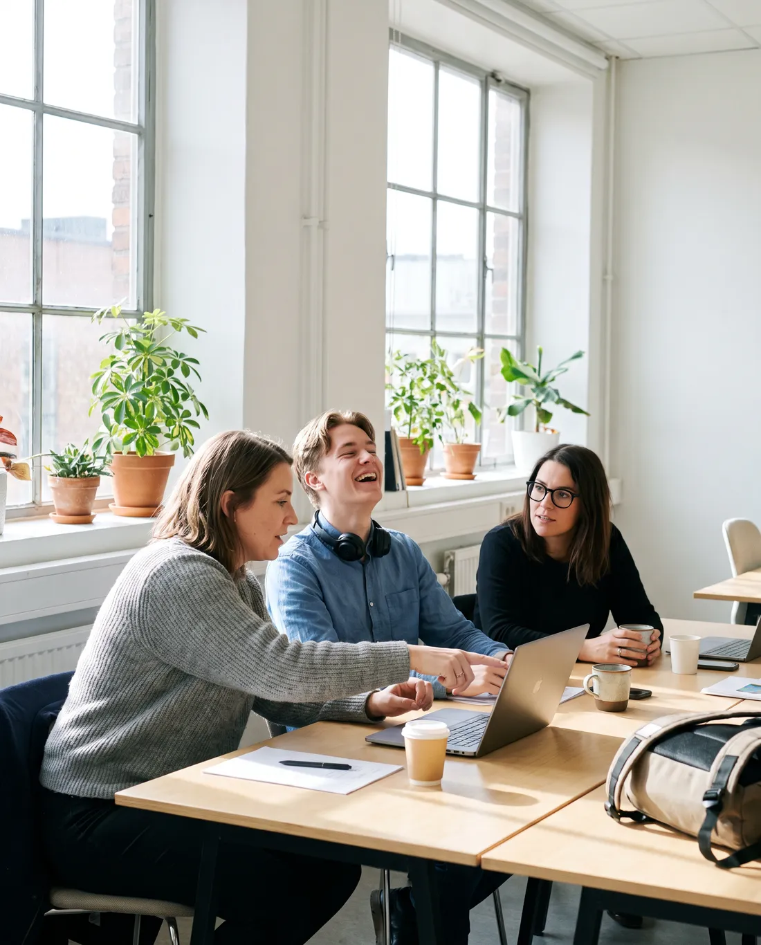 Tre kollegor på ett ljust kontor samlade runt en laptop